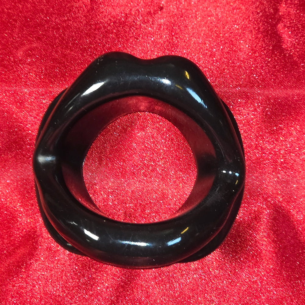 Öppen Mun Gag i svart silikon, framifrån på röd glitterbakgrund. O-ring gag för BDSM och kinky lek från Chambers of Love.