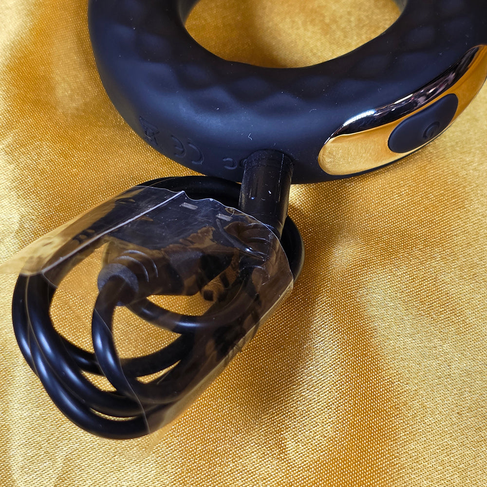 Penisring med 10 vibrationer med ansluten USB-laddkabel och LED-laddindikator på guldfärgad bakgrund från Chambers of Love
